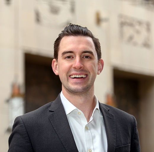 erics professional headshot smiling wearing a grey suit and white undershirt