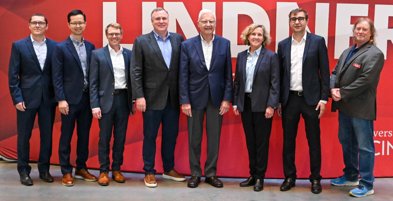 Seven men and one woman in professional dress pose in front of a banner.