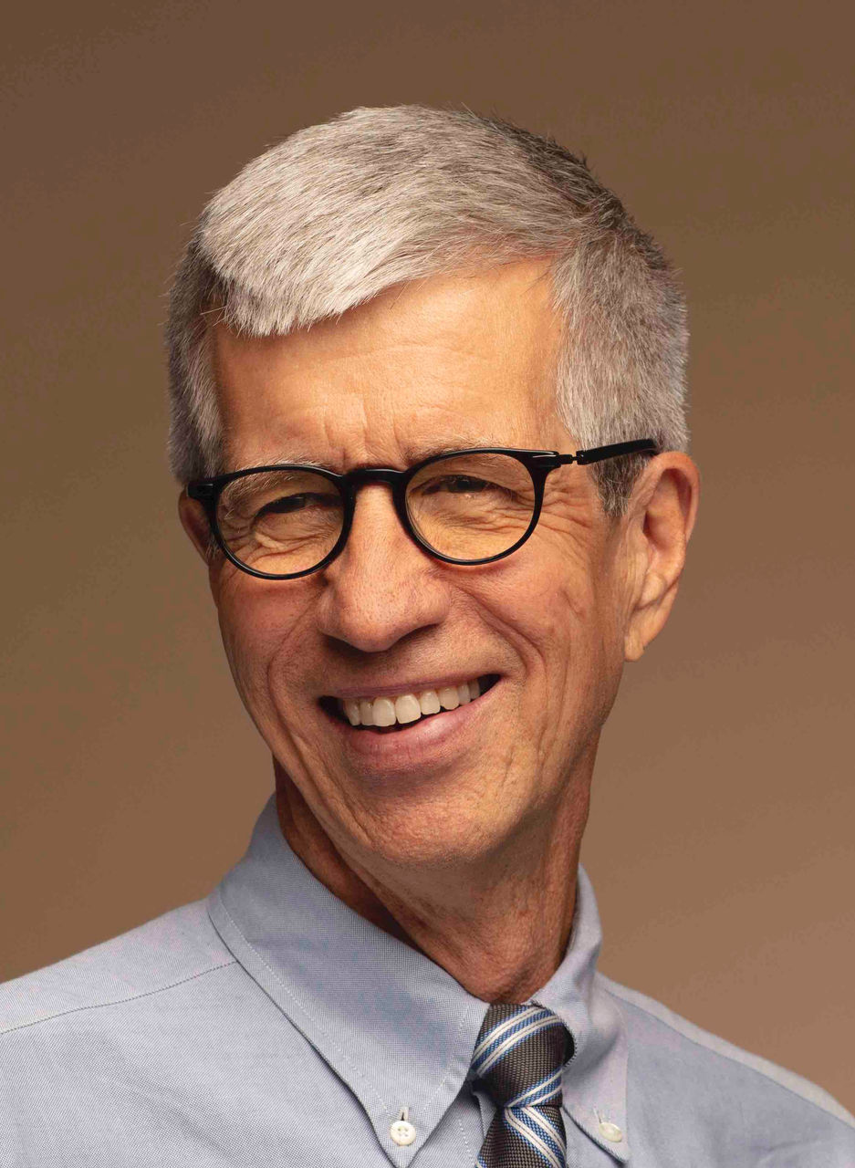 A man in glasses wears a gray shirt and tie.