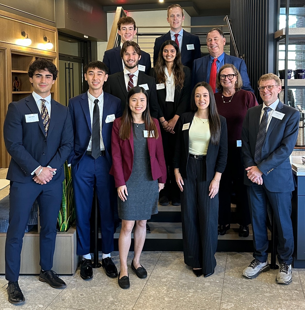 A group of students and professionals in professional clothing stand on and near a staircase.
