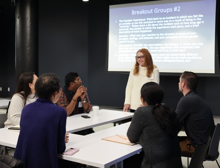 A woman stands in front of table of workshop participants.