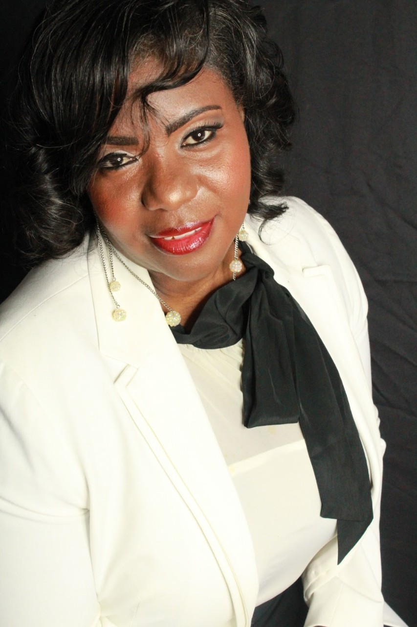 A woman wears a white suit with a black scarf.