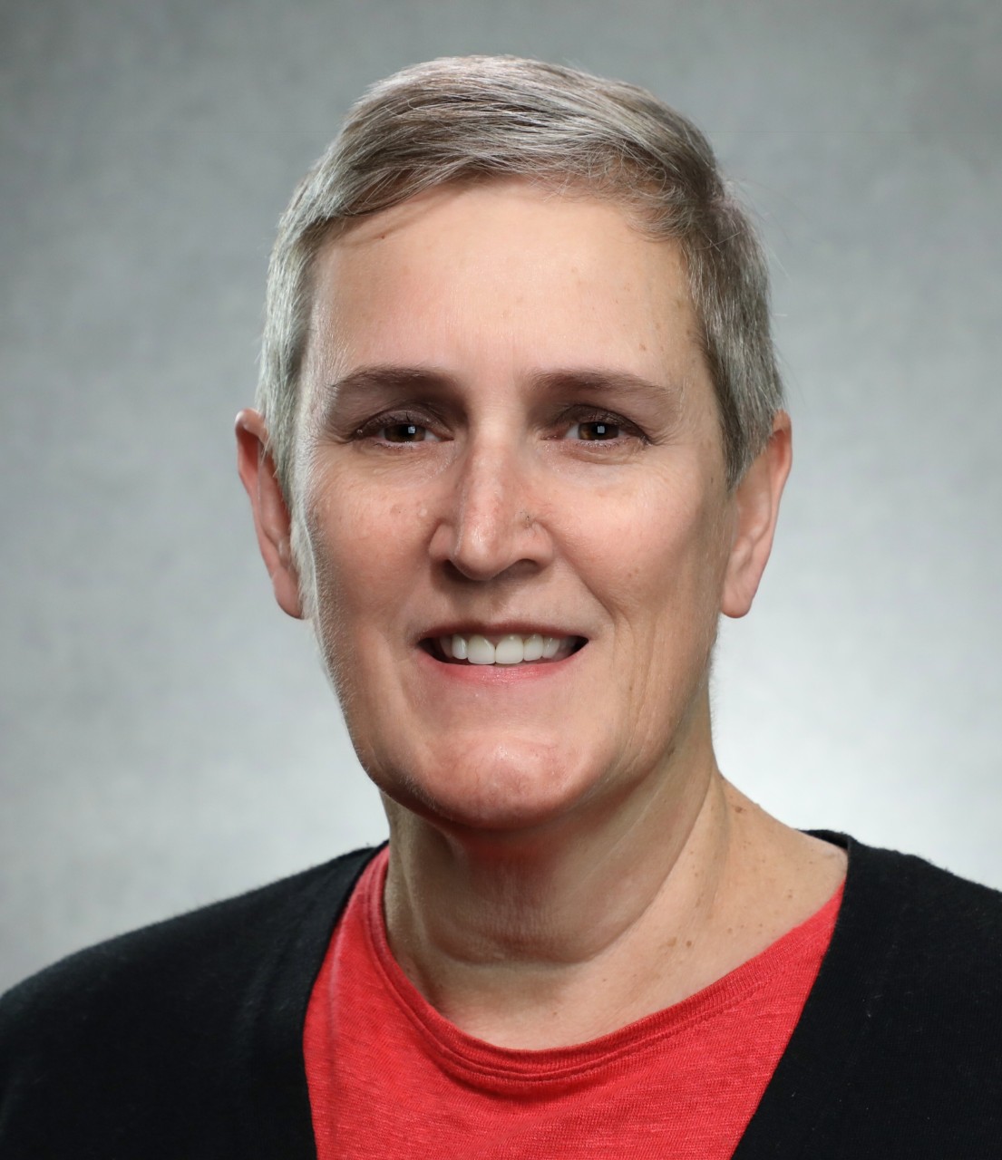 A woman wearing a black coat and red shirt smiles.
