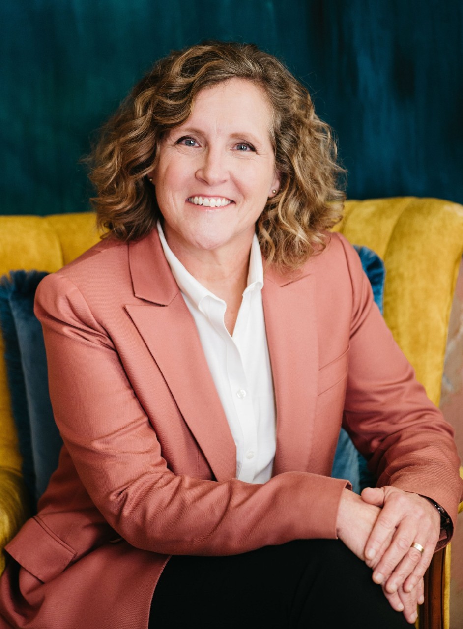 A woman smiles in a salmon colored jacket and white shirt.