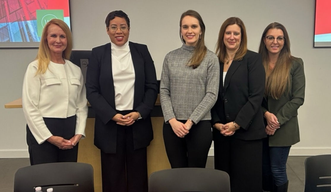 Five women stand in professional dress in a Lindner classroom.