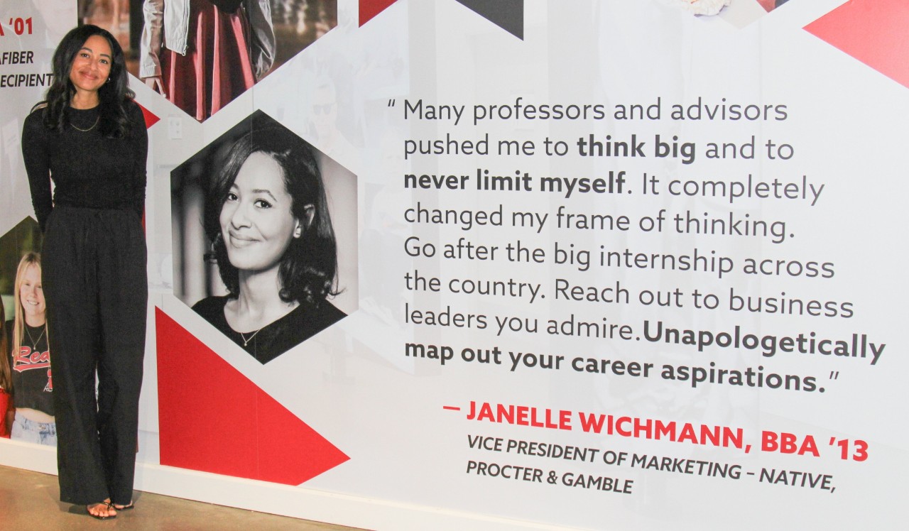 Janelle Wichmann stands in all black next to her likeness on a wall graphic.