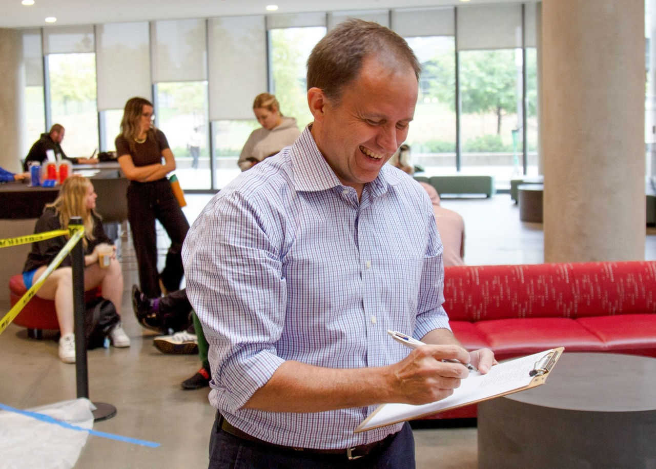 Craig Froehle writes on a clipboard in the Lindner Hall atrium.