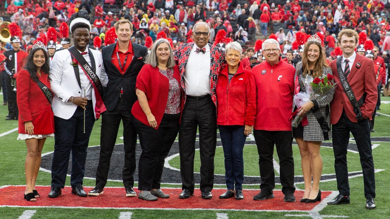 The Homecoming court, dressed a variety of reds, grays, whites and blacks, stand on a field.