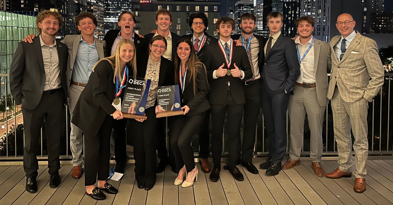Students hold a trophy and smile in professional dress on a rooftop.