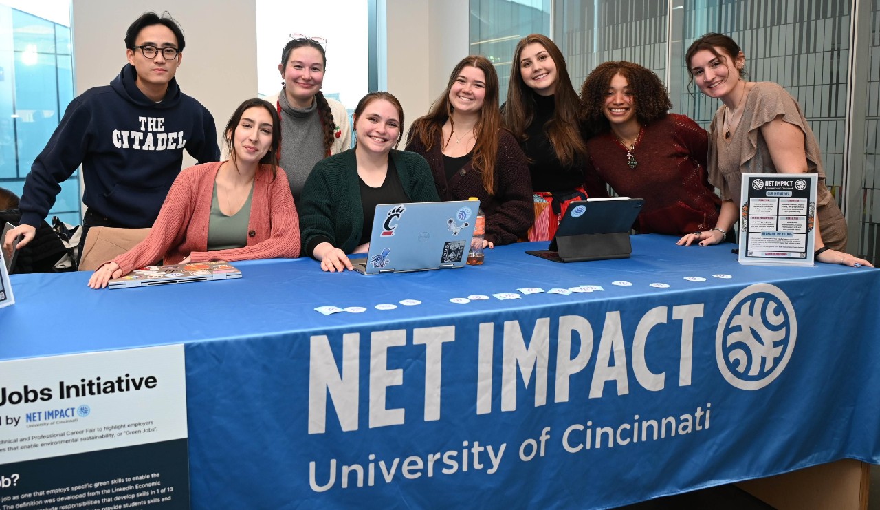 Students sit and stand behind a blue and white banner.