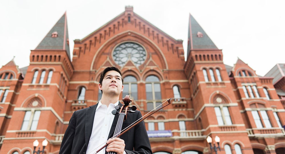 Jonathan Lee standing with his cello in front of Cincinnati's Music Hall