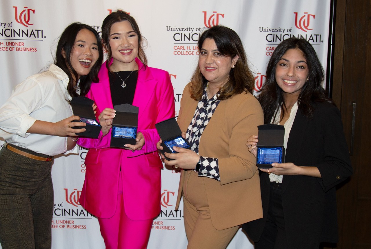 four women in business attire at a Lindner MBA graduation reception holding gifts