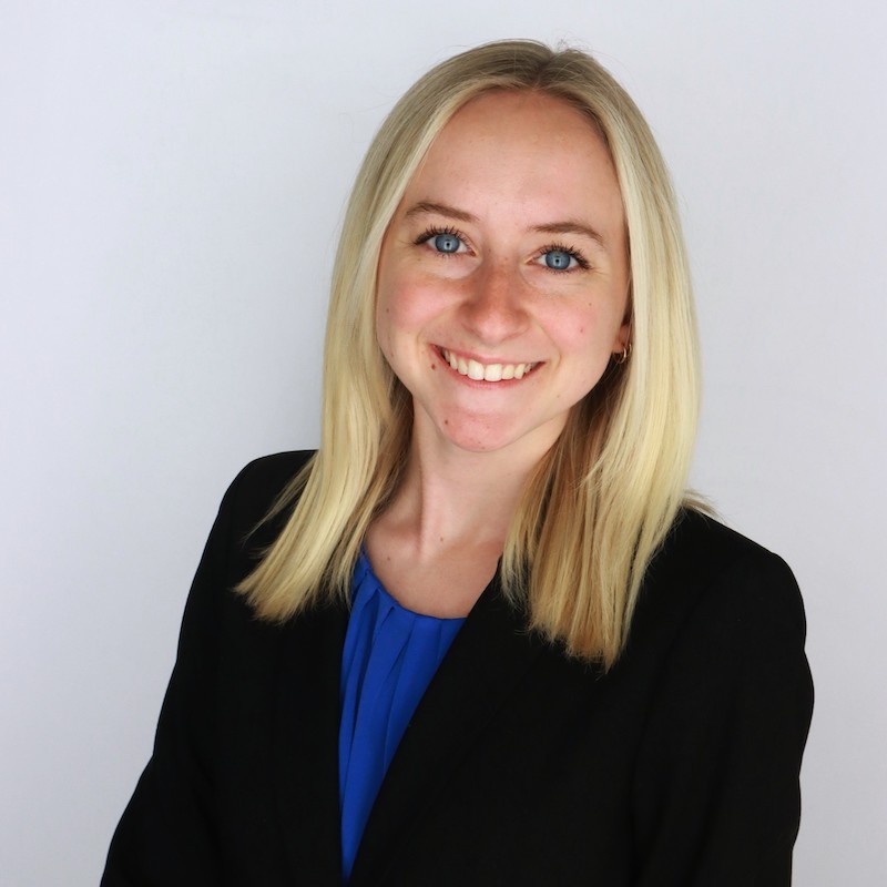 Headshot of Lacey Kelly in a blue blouse and black suit jacket in front of grey lit background