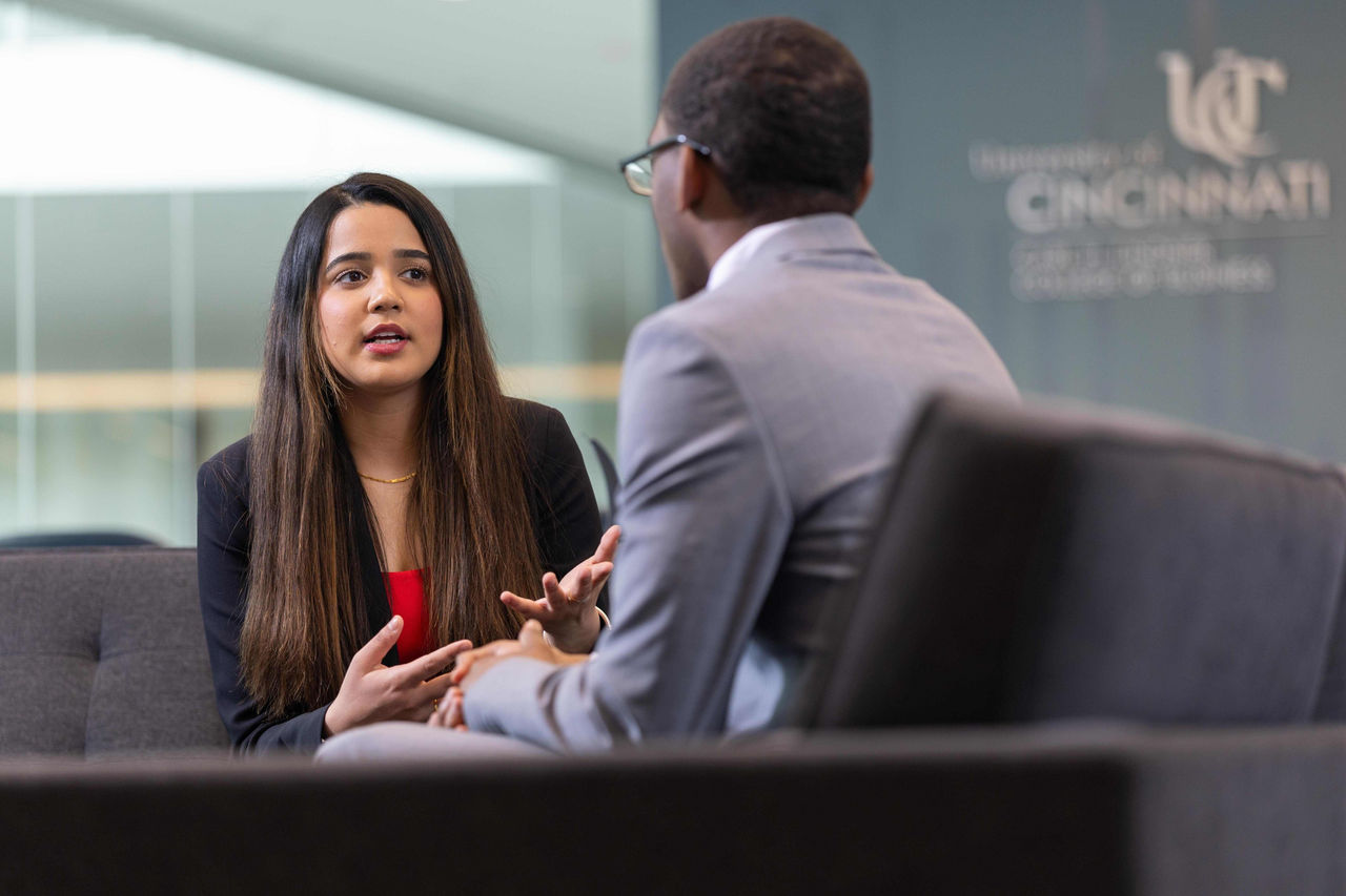 A male and a female student sit across from each other in professional dress, engaging in coversation.