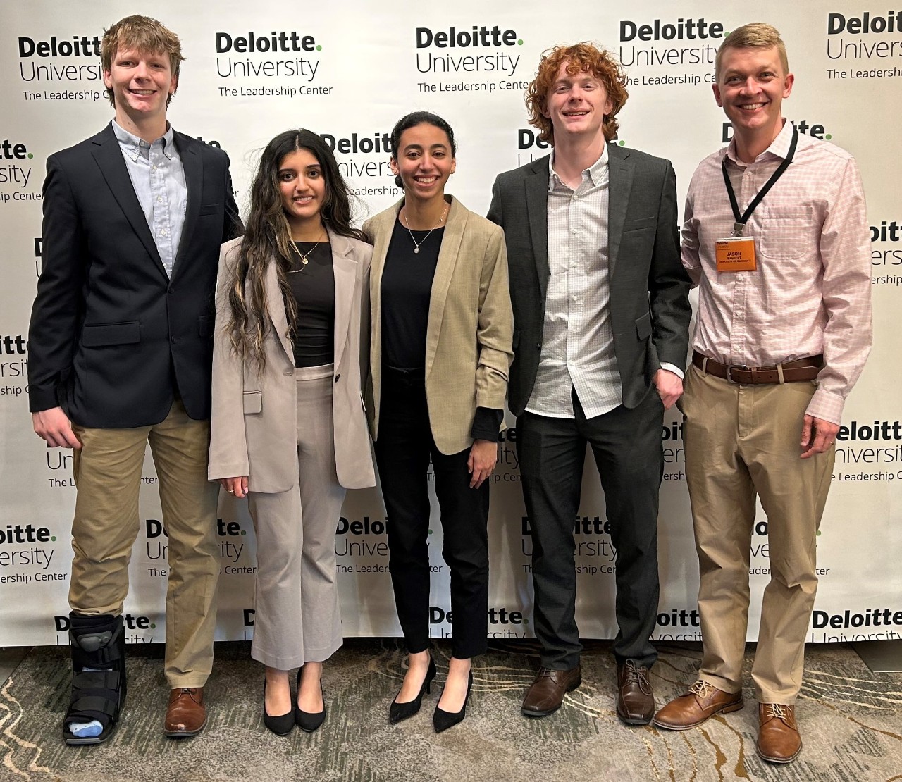 Four students and a professor in professional dress pose for a picture in front of a white back drop.