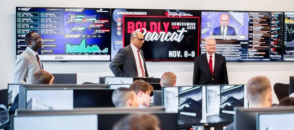 Prof. Charles Appeadu, UC President Neville Pinto, and Tim Johnson in front of students in the investment lab