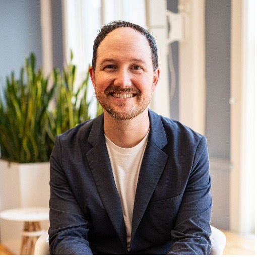 A man in a dark blue suit and white shirt smiles.