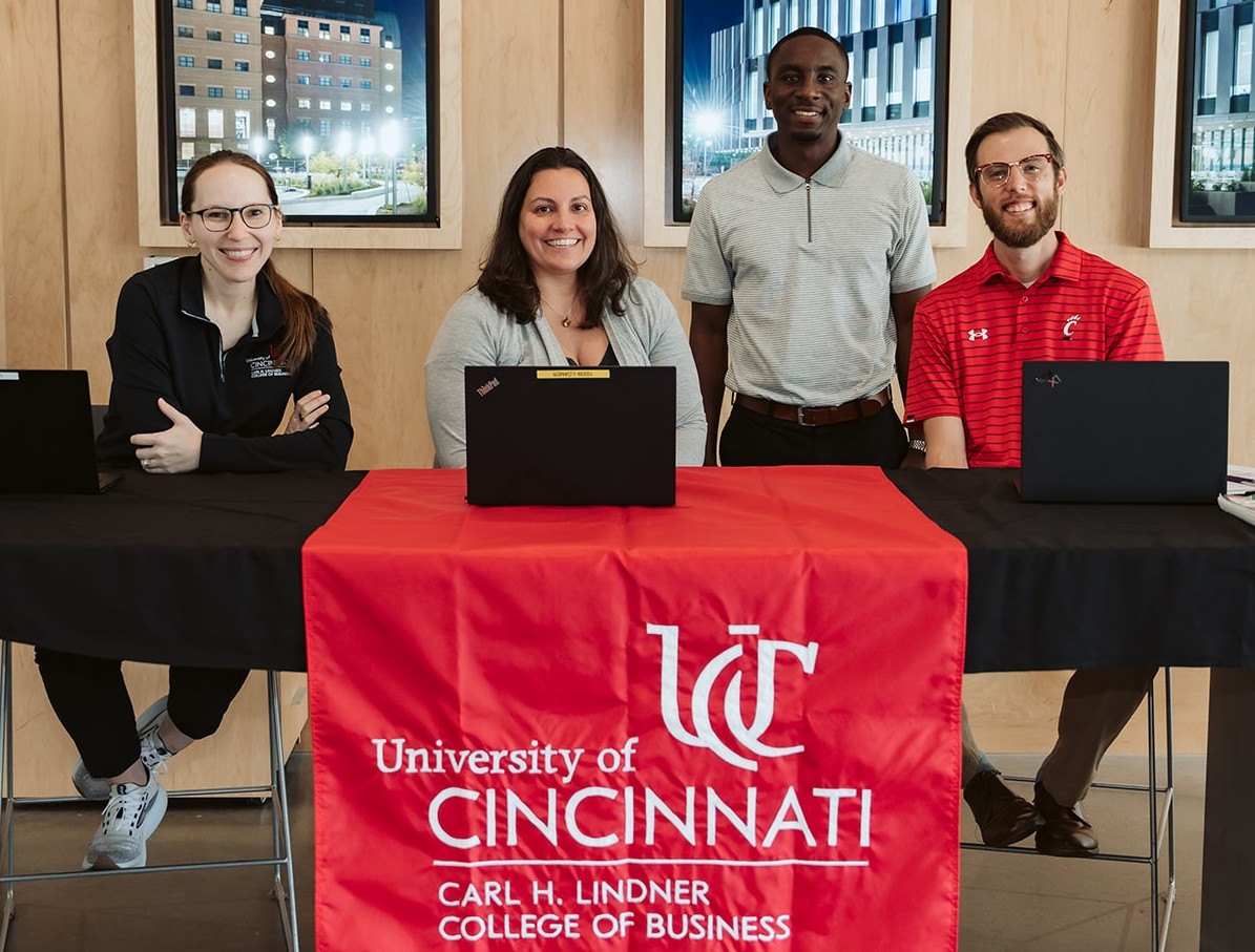 Four people, three seated and one standing, smile from behind a table with a Lindner banner.