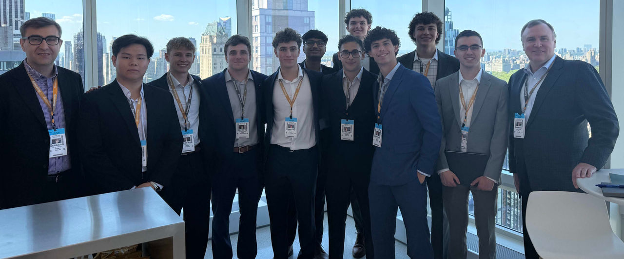 A group of students and two program advisors pose in front of a large glass wall.