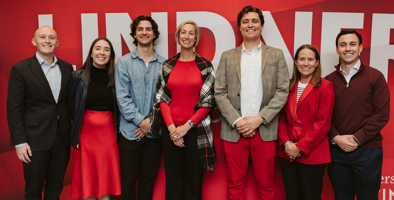 Men and women in professional dress stand in front of a red and white banner.
