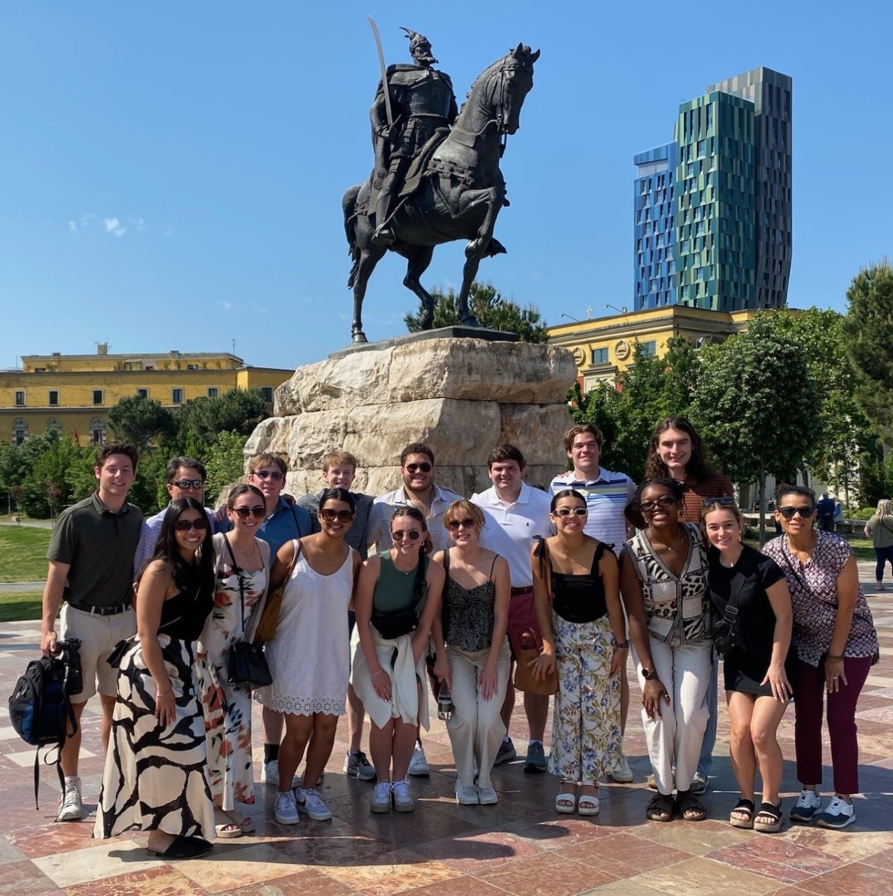 Seventeen Lindner Business Honors students pose in front of a statue of a man riding a horse in a park plaza