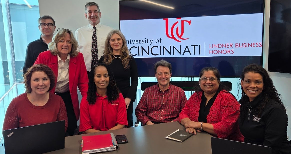 A group of Lindner faculty and staff members dressed in red, white and black sit and stand around a table.